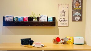 A small café with a wooden table, two white bar stools, a coffee machine, and a shelf with books and a coffee-themed poster. - myRoom at 14 J Mandalay (George Town)