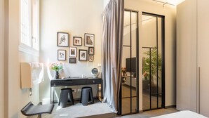 Una habitación de hotel moderna con una cama grande, un escritorio con dos taburetes, un tocador con espejo y un ventanal corredero que da a un balcón.