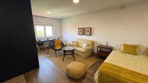 A room with a bed, a sofa, a small table, a chair, and a window.