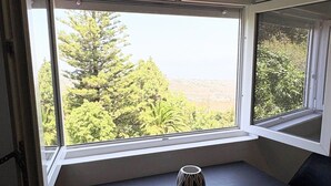 Ein Zimmer mit einem Tisch und zwei Stühlen, ein Fenster mit Blick auf Bäume und Hügel, und eine kleine dekorative Vase auf dem Tisch.