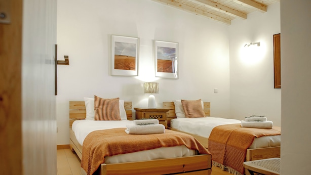 Un dormitorio con dos camas, una mesita de noche, una lámpara y techo de madera.