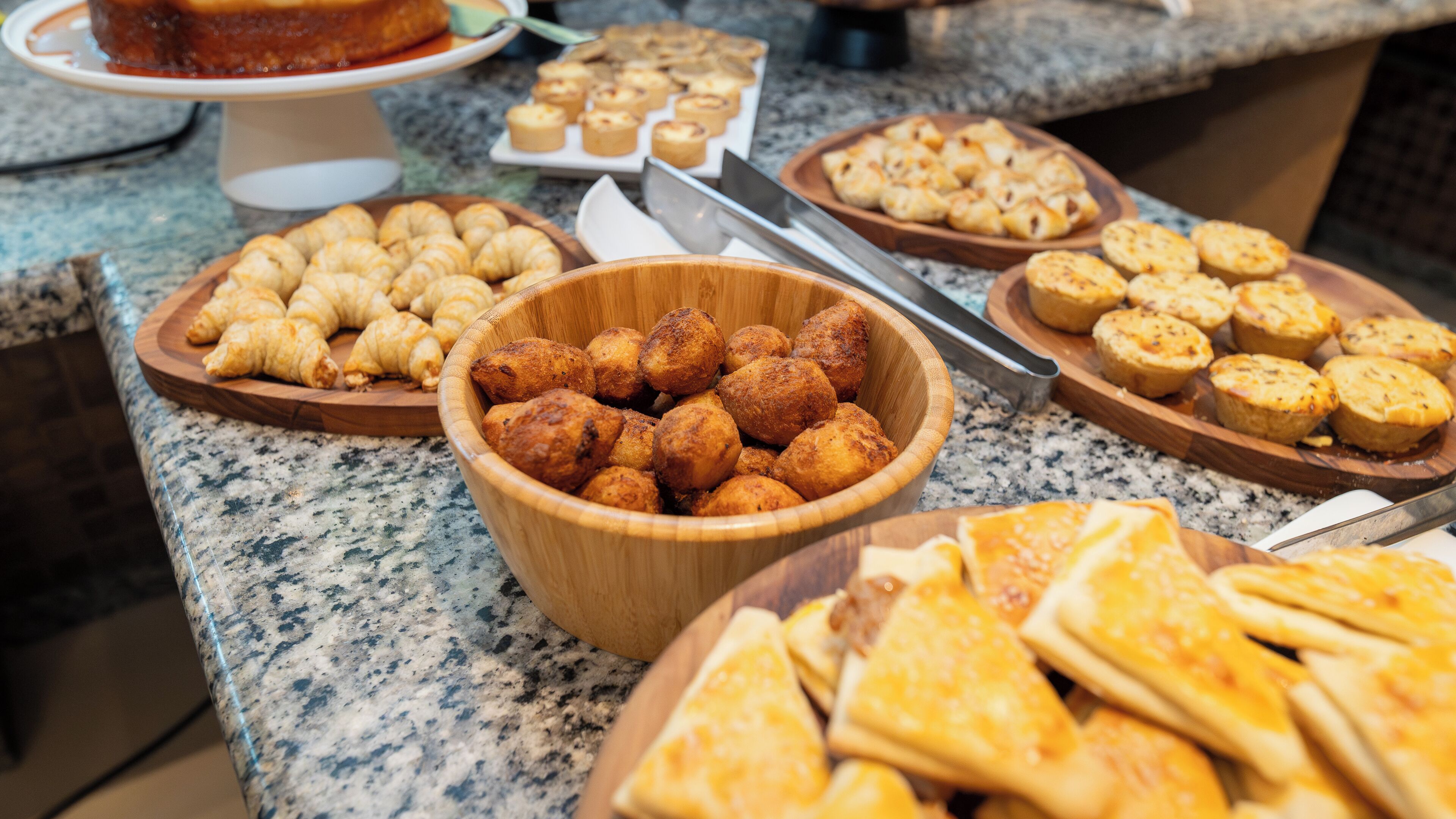 Una mesa de buffet con una variedad de productos horneados, como croissants, muffins y rebanadas de queso.
