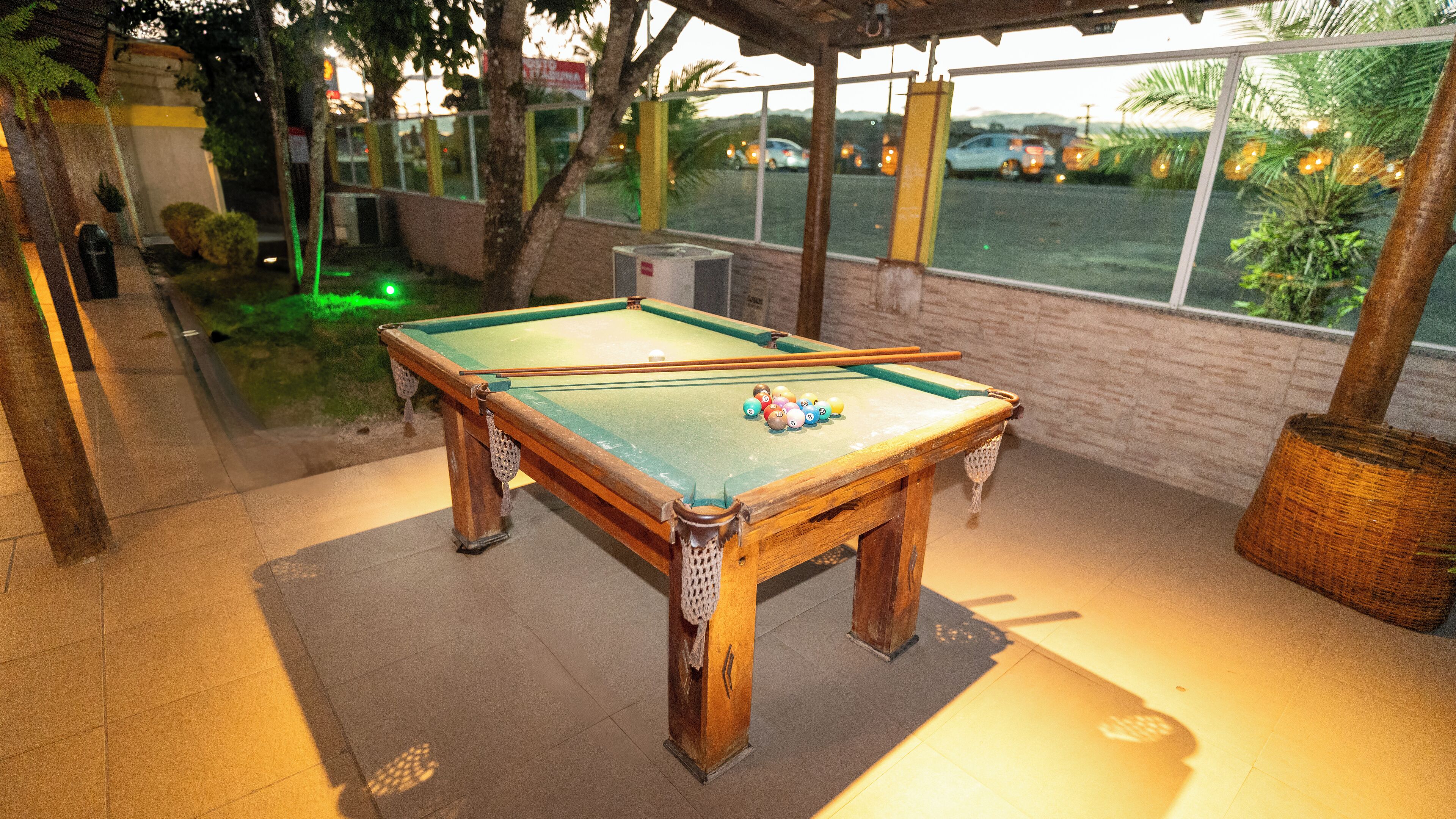 A pool table with balls, a wicker basket, and a window with a view of parked cars.