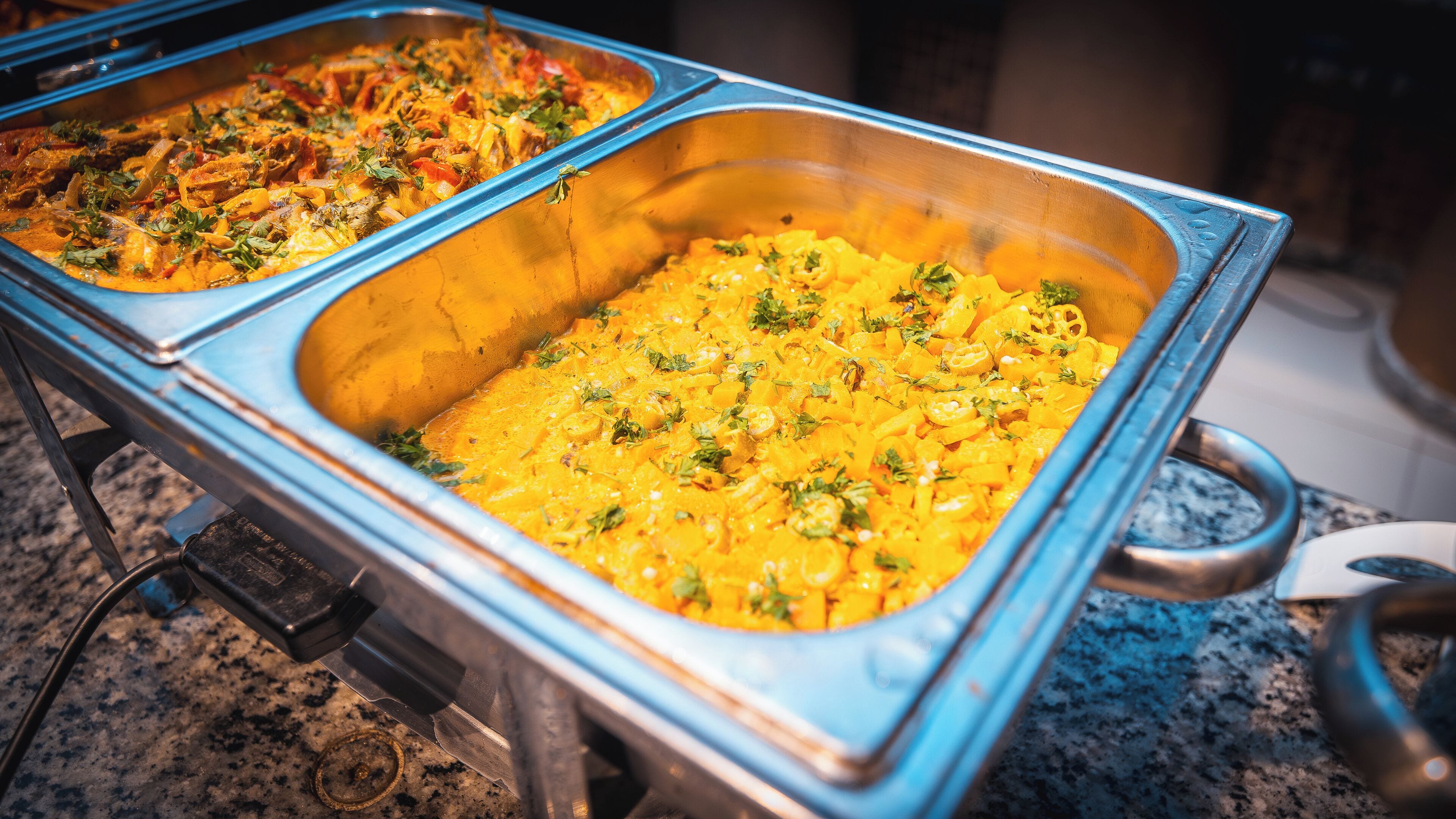 Een buffet met twee grote metalen opschepkommen, gevuld met diverse gerechten.