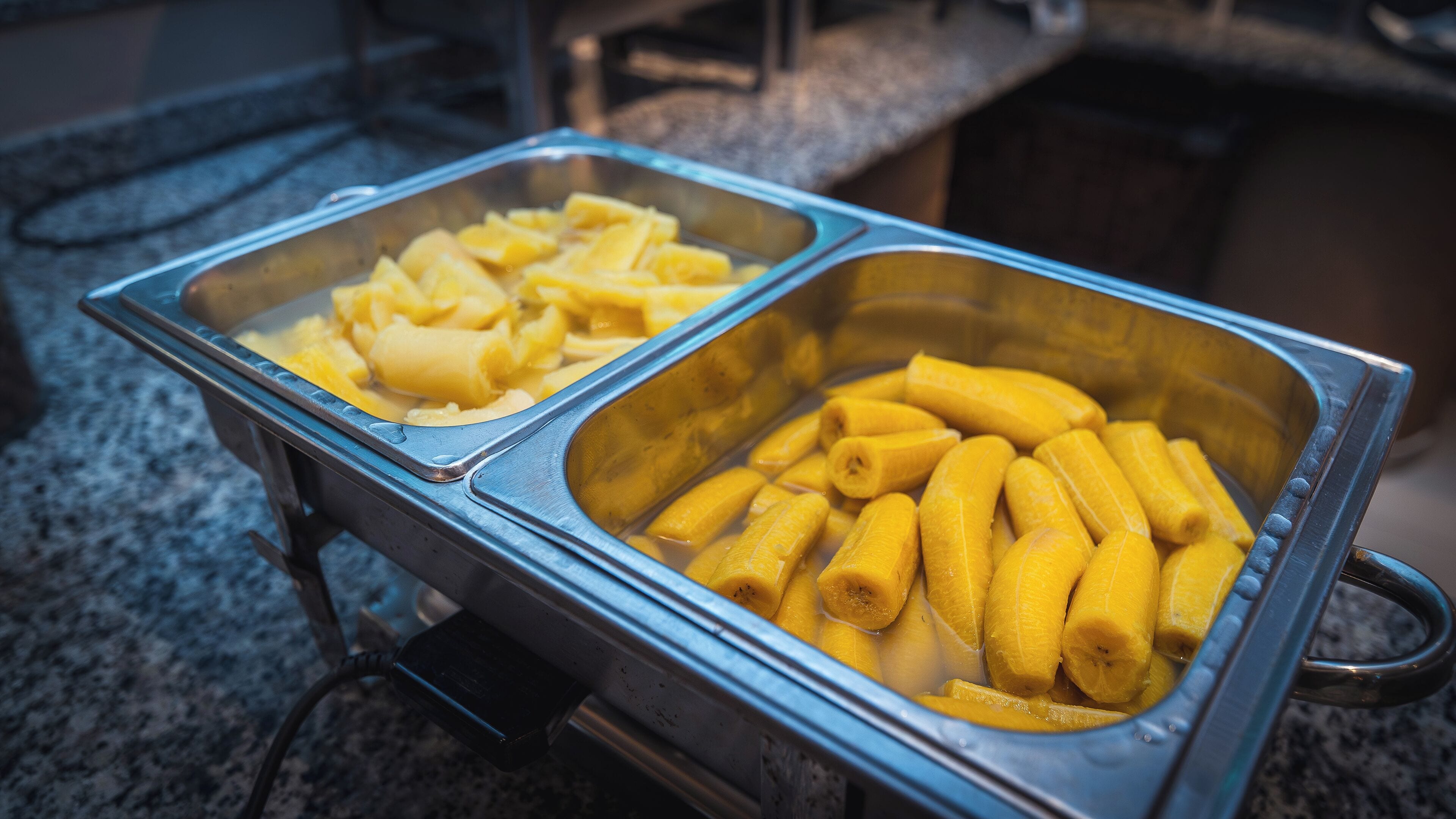 A buffet with two metal trays, one containing sliced bananas and the other containing whole bananas.