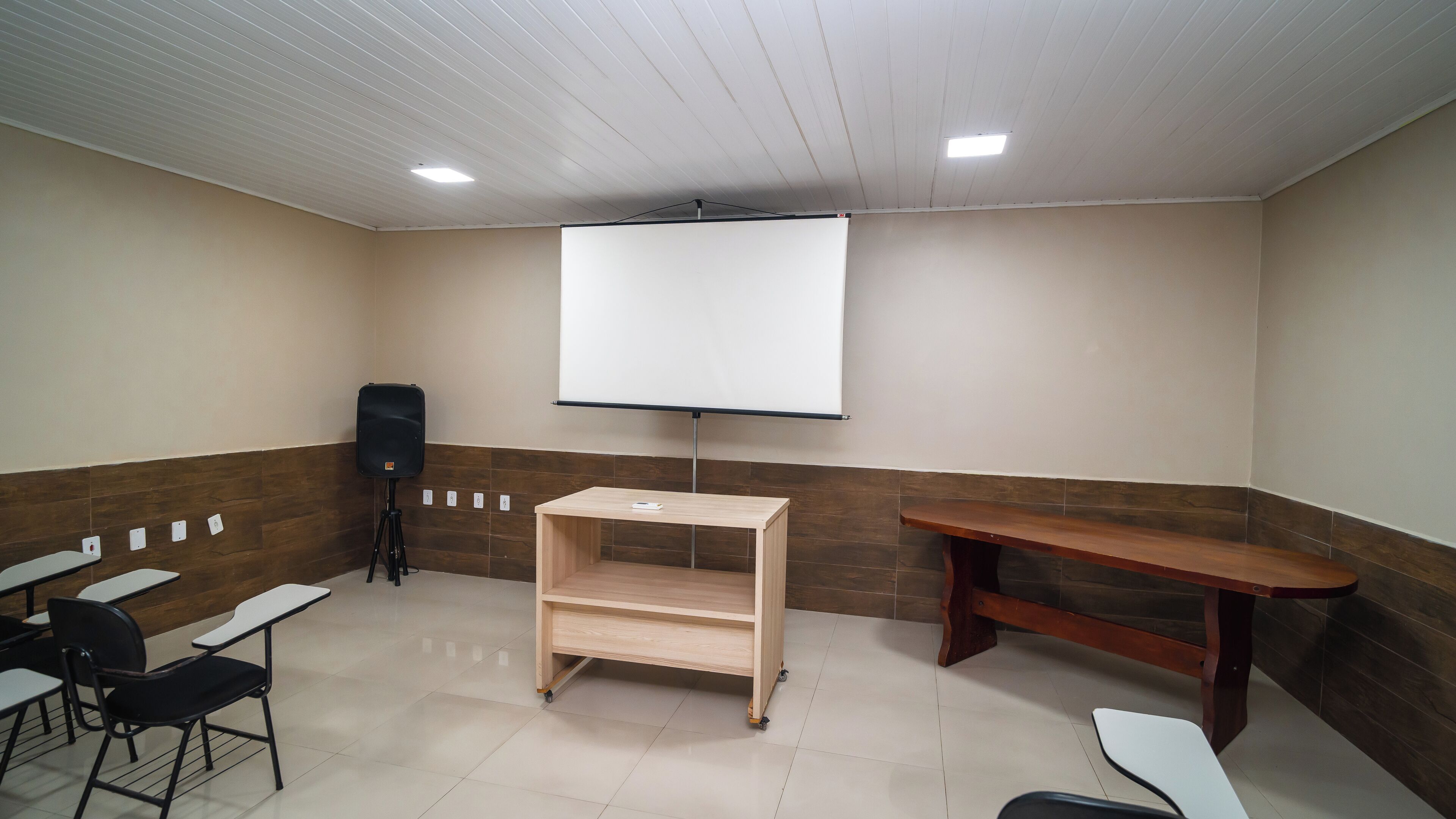 A conference room with a projector screen, a speaker, and a wooden table.