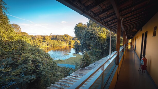 A view from a covered balcony overlooking a lake surrounded by dense foliage. - Pousada Itajuipe (Itabuna)