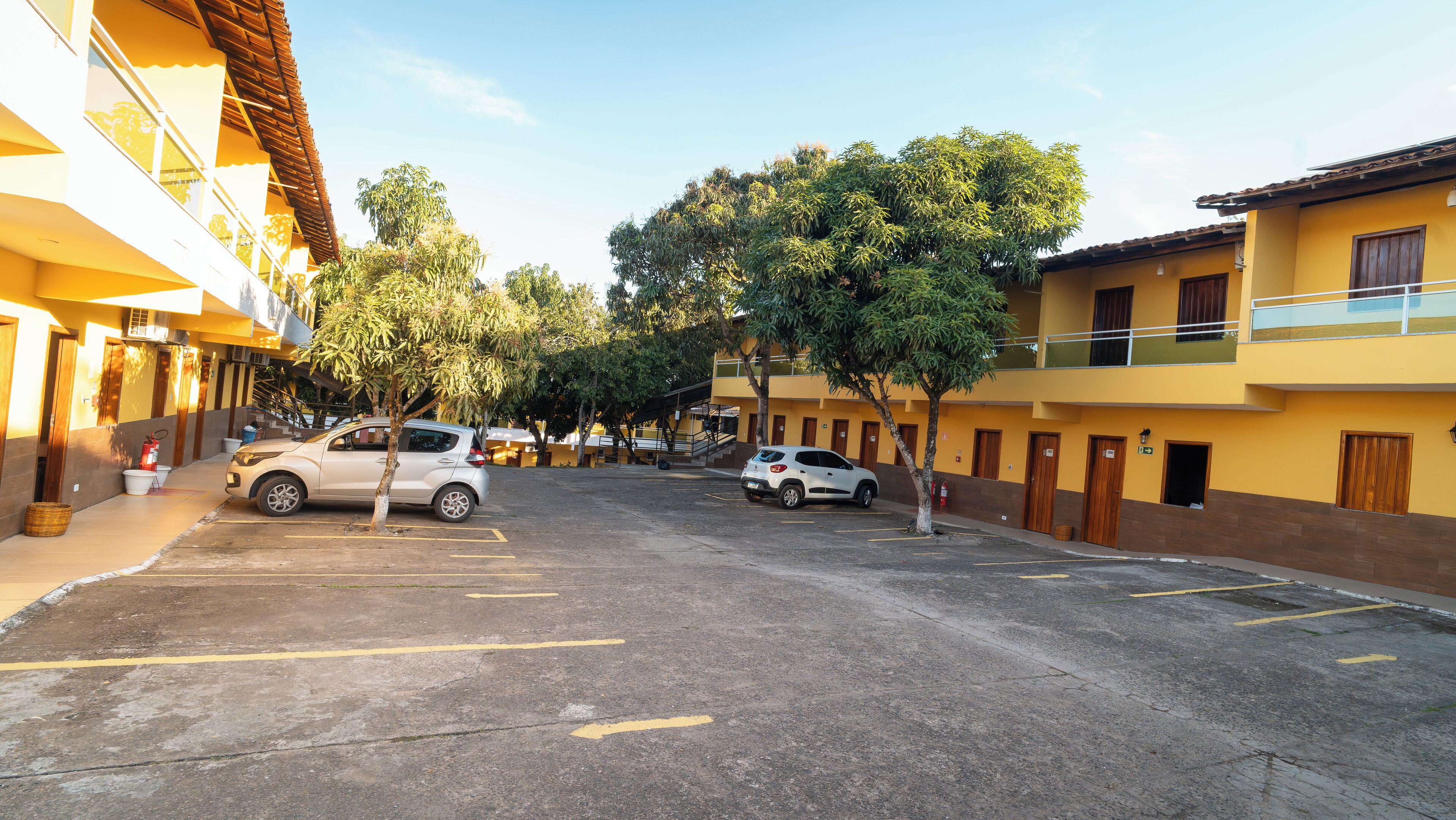 Un parking avec deux voitures, des arbres et des bâtiments jaunes dotés de balcons.