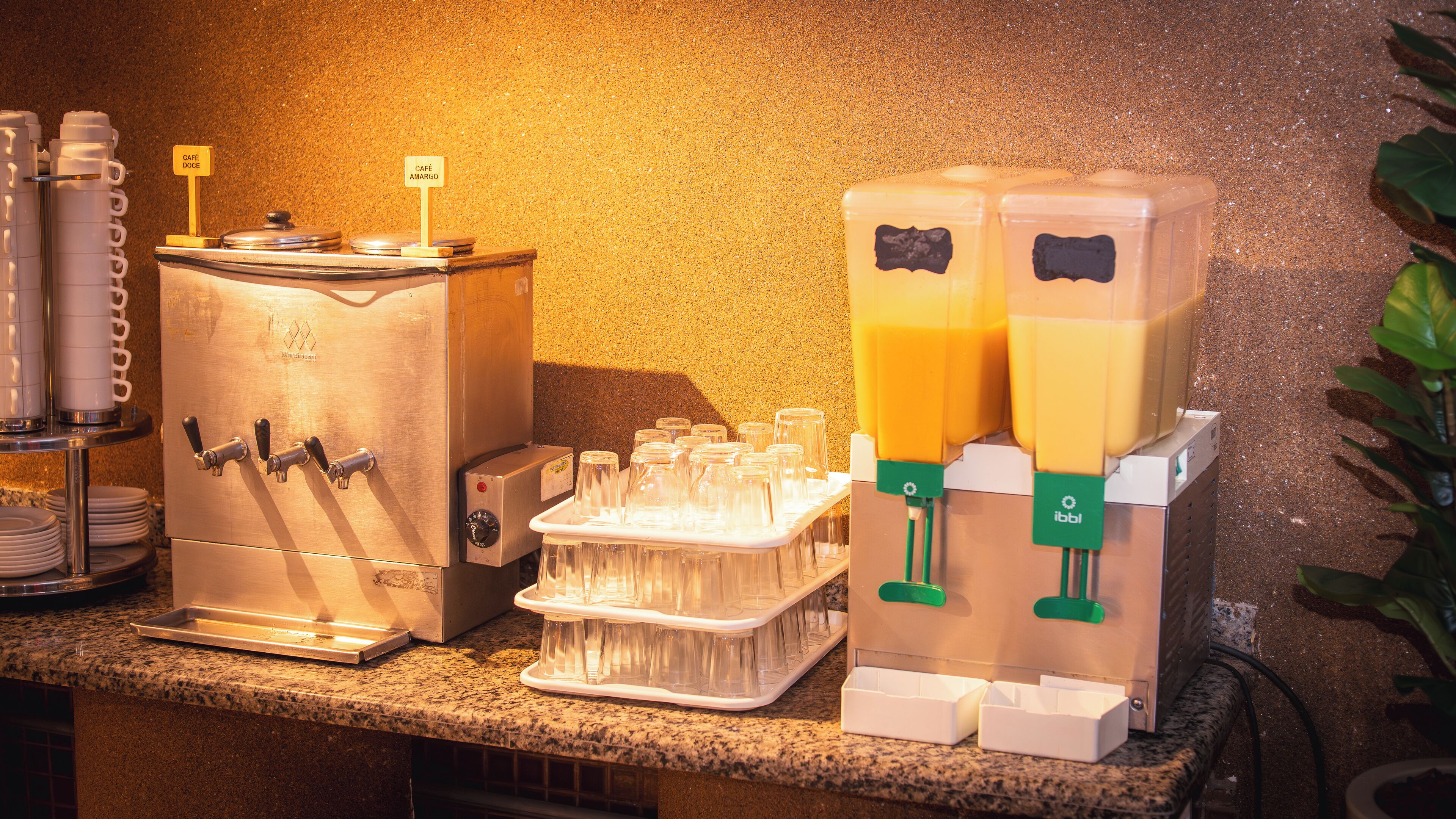 A beverage station with dispensers, a tray of glasses, and a sign indicating 'Café Amargo'.
