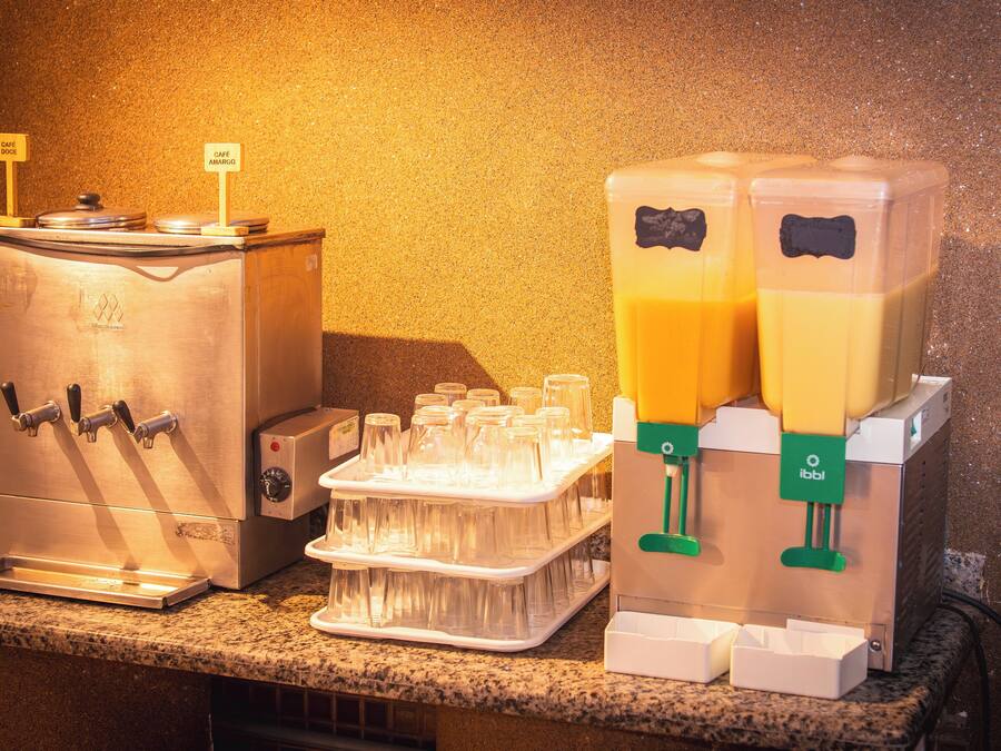 Una estación de bebidas con dispensadores, una bandeja de vasos y un cartel que indica 'Café Amargo'.