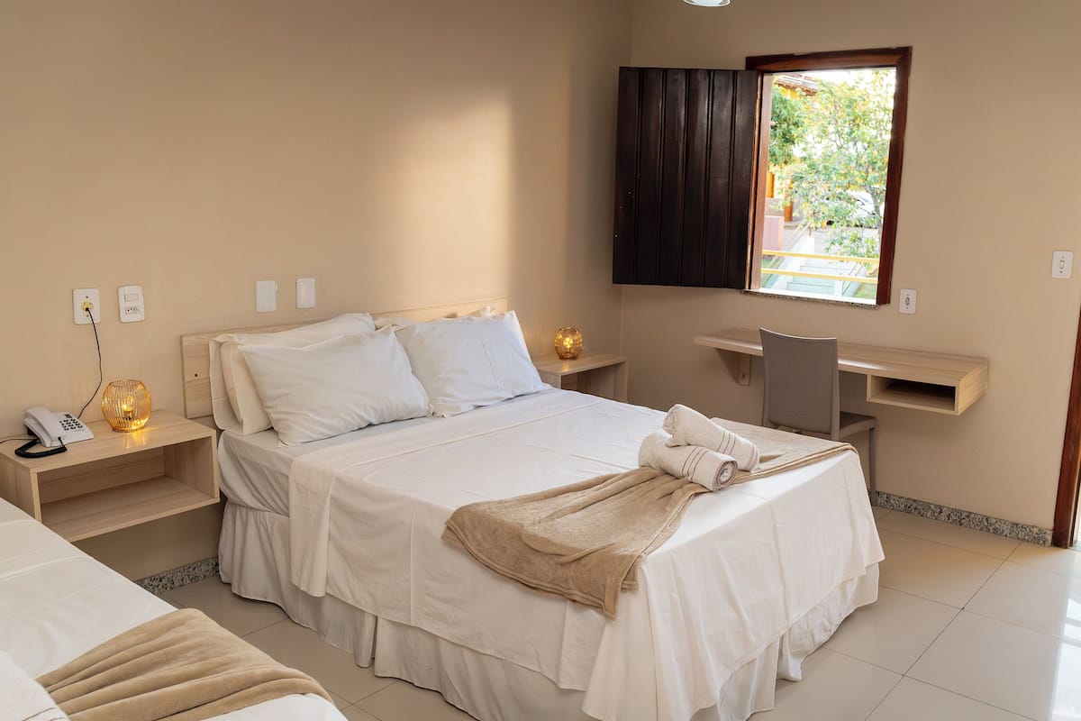 A hotel room with a bed, bedside tables, a desk, a chair, a TV, and a window with a view of the outside.