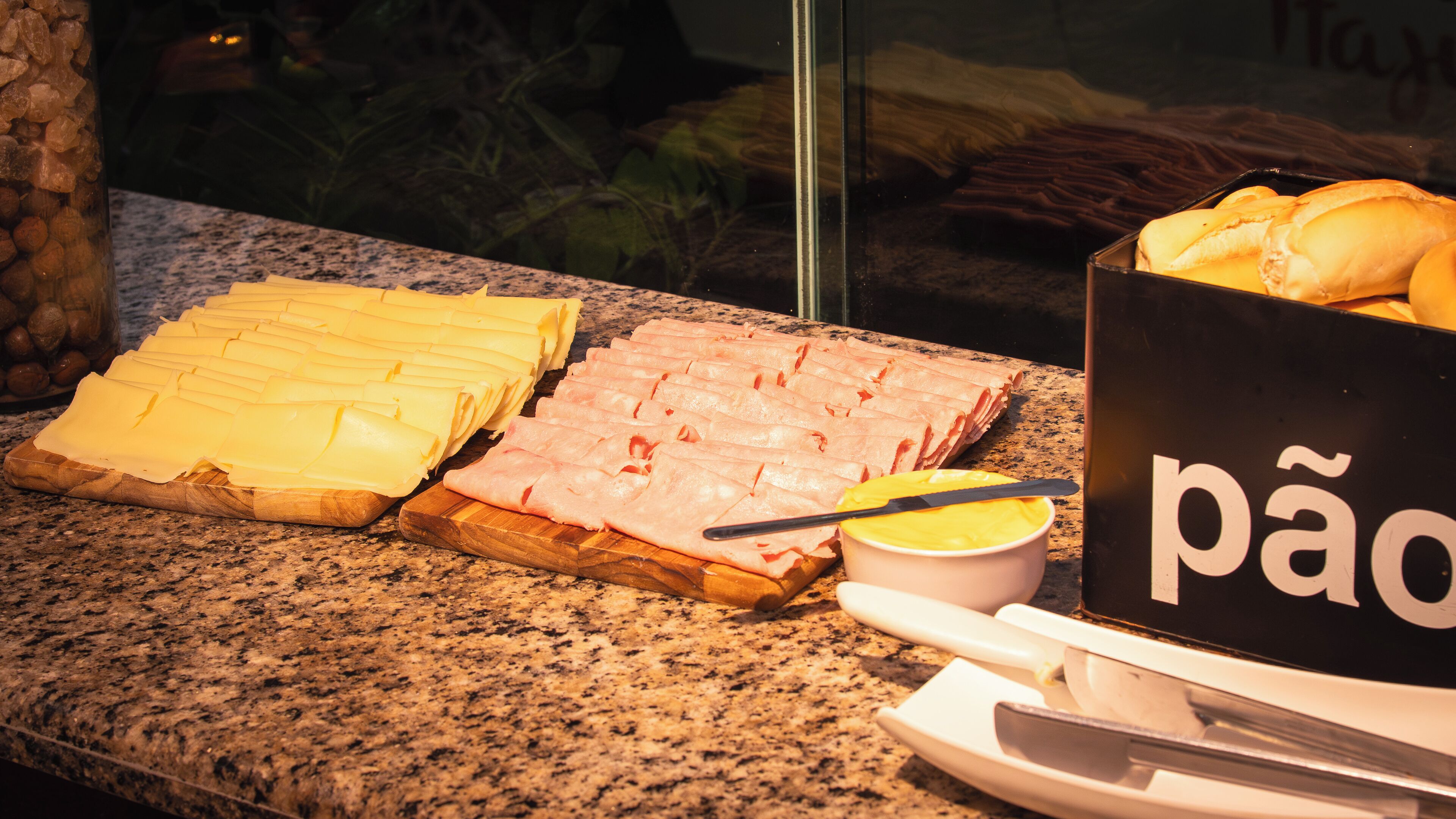 Una mesa de buffet con queso en rodajas, jamón y un bol de crema amarilla.