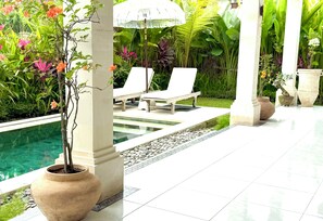 A poolside area with lounge chairs, a potted plant, and a decorative umbrella. - Villa Hummingbird Ubud (Ubud)