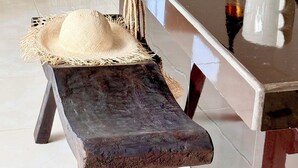 A modern kitchen with a long countertop, a bench, and a dining area with a sofa and cushions. - Villa Hummingbird Ubud (Ubud)