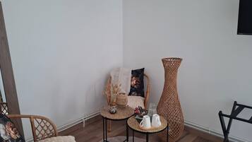 A room with a wicker chair, a small table with cups, a tall vase, and a flat-screen TV mounted on the wall.
