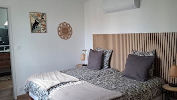 A bedroom with a bed, bedside tables, a mirror, and a wall-mounted air conditioner.