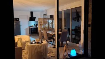 A modern living room with a dining area, a kitchen, and a sliding glass door leading to an outdoor area.