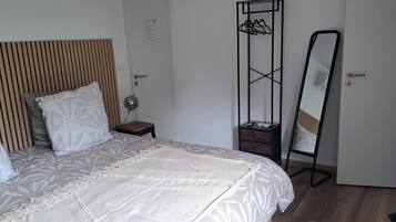 Una cama bien hecha con colcha estampada, una lámpara de noche, un cabecero de madera, un armario con espejo y una mesita de noche.
