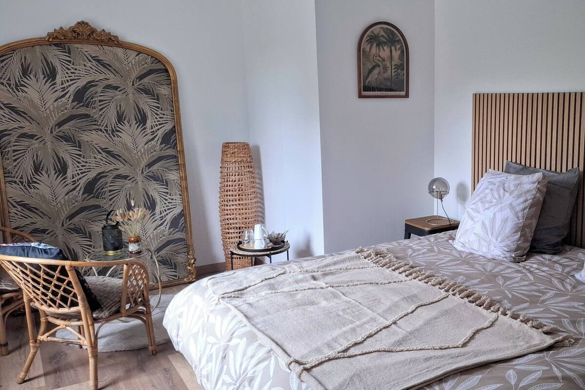 A bedroom with a bed, a chair, a mirror, a lamp, and a wall-mounted picture.