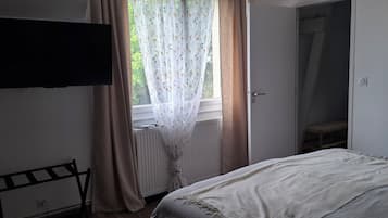 Un dormitorio con cama, radiador, televisión montada en la pared y ventana con cortinas.