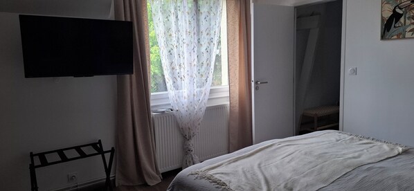 A bedroom with a bed, a radiator, a television mounted on the wall, and a window with curtains.
