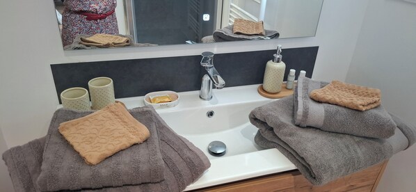 Un baño con un lavamanos blanco, un espejo encima y dos toallas sobre él.