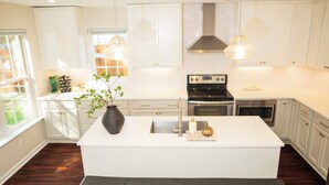 A modern kitchen with white cabinetry, stainless steel appliances, and pendant lighting.