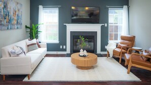 A living room with a white sofa, a round coffee table, a leather armchair, and a fireplace.