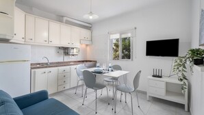 A modern kitchen with white cabinets, a dining table with chairs, a built-in oven, and a flat-screen TV mounted on the wall. - Vacation 'Beach View Playa Los Cristiano' with Sea View and Wi-Fi (Arona)