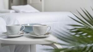 A bed with white bedding, a white table with two cups and saucers, and a green plant in the foreground. - Vacation 'Beach View Playa Los Cristiano' with Sea View and Wi-Fi (Arona)