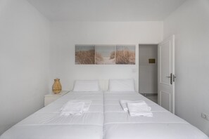 Un letto matrimoniale con biancheria da letto bianca, un comodino con un vaso e una porta che conduce in un'altra stanza.