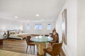 A spacious bedroom with a large bed, a glass-top dining table, and a seating area with chairs.