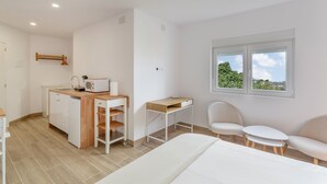 Une chambre comprenant un lit, un bureau, une chaise, une petite table, un four à micro-ondes, un évier et une fenêtre donnant sur un beau paysage.