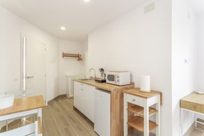 Una pequeña cocina con armarios blancos, una encimera de madera, un microondas, un fregadero y un refrigerador pequeño.