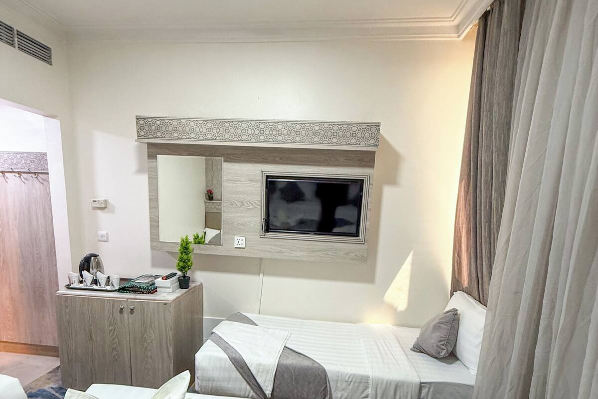 A hotel room with two beds, a TV, a desk, and a mirror.