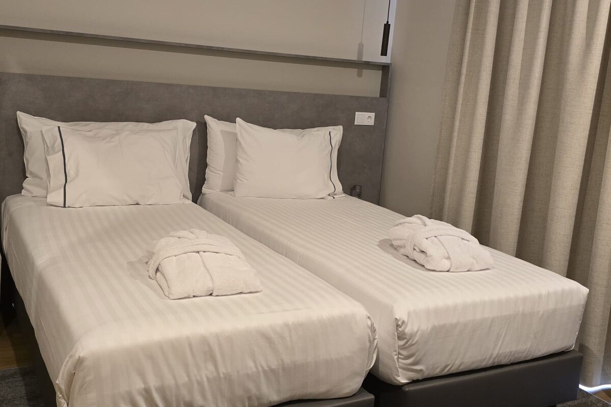 A hotel room with two beds, a grey headboard, and a grey carpet.