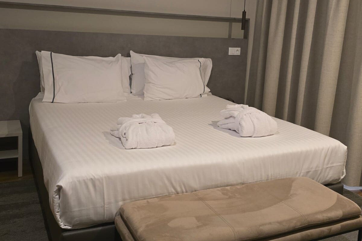 A hotel room with a bed, pillows, a bench, and a curtain.