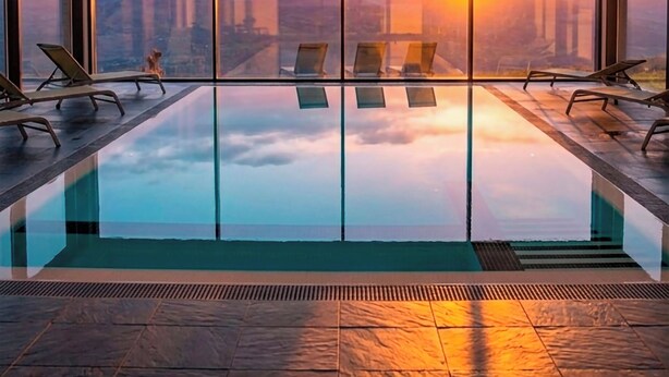 Una piscina interior moderna con una vista panorámica del atardecer sobre montañas.
