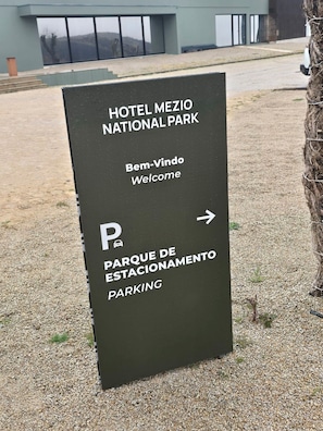 Schild für das Hotel Mezio Nationalpark mit einer Willkommensbotschaft und Wegweiser zum Parkplatz.