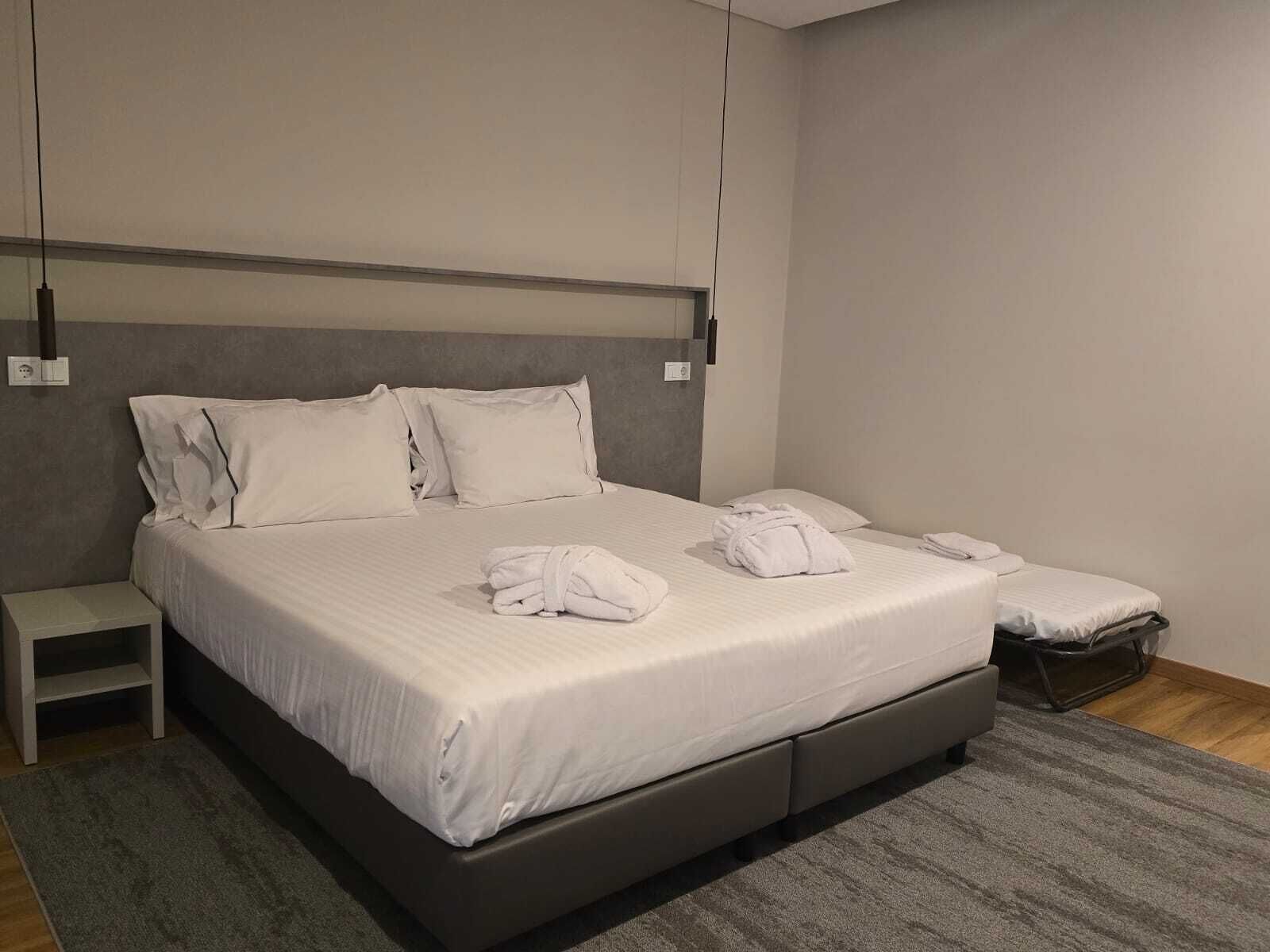 Una habitación de hotel moderna con una cama grande, una mesita de noche y un pequeño banco.