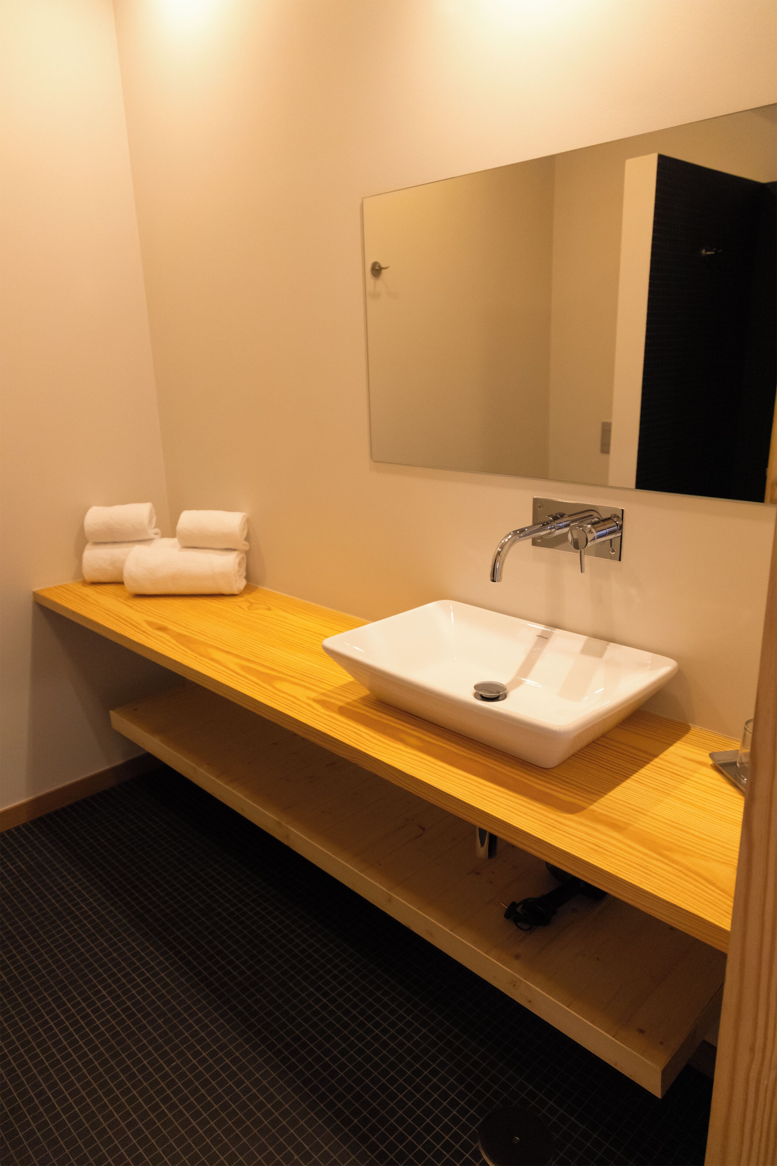 Un baño con lavamanos blanco, tocador de madera, espejo y toallero con toallas.