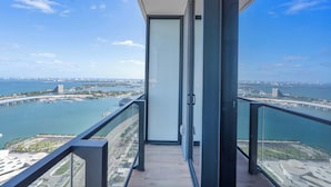 A balcony with a glass door leading to a room, overlooking a coastal cityscape with a bridge and marina. - Downtown Suite with Luxe Pool & Beach Club (Miami)