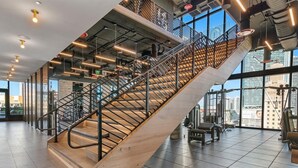 A modern indoor space with a central staircase, large windows, and gym equipment. - Downtown Suite with Luxe Pool & Beach Club (Miami)