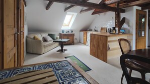 Un espai tipus loft amb sostre alt, bigues de fusta a la vista, petita cuina, sofà, taula de dinar i una illa petita amb rentapelats.