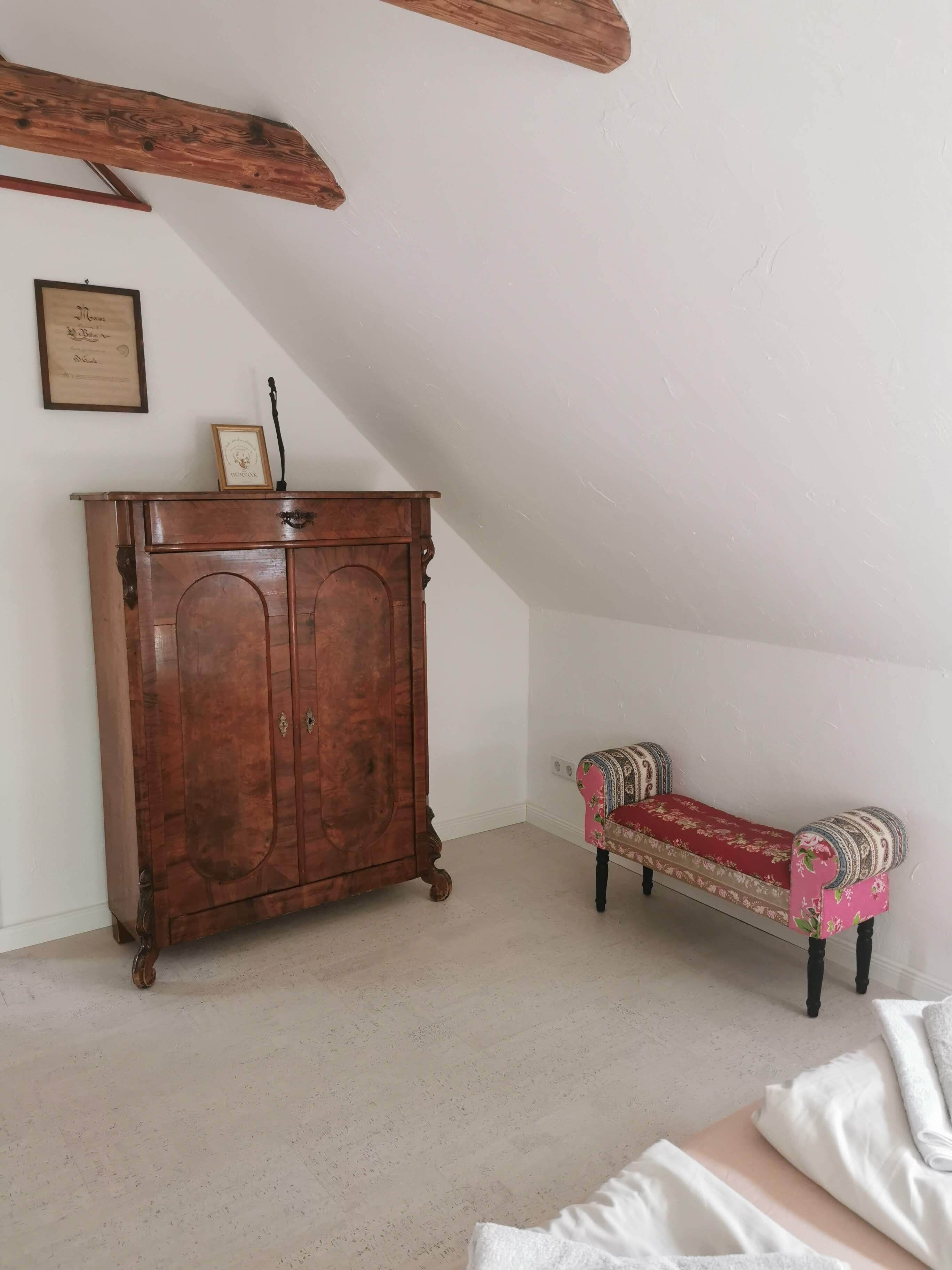 Ein Zimmer mit einem Holzschrank, einem gemusterten Sofa und einer weißen Wand.