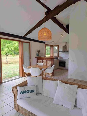 A cozy living area with a wicker sofa, a dining table with white chairs, and a hanging light fixture. - House in Léon, swimming pool, sports and games room, large garden, 5 minutes from the lake (Léon)
