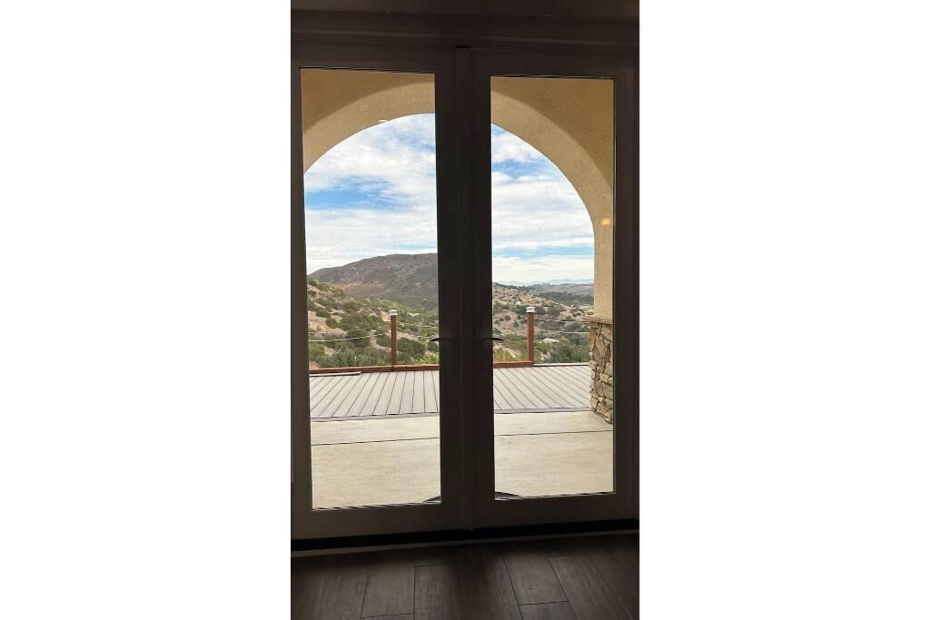 Une vue à travers une porte donnant sur un balcon, qui offre une perspective sur un paysage vallonné.