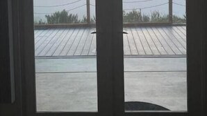 En vy genom ett fönster med en träveranda och ett staket av metall.