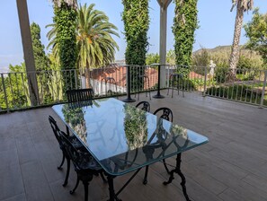 Una mesa con cubierta de vidrio y sillas en un balcón con vistas a zonas verdes y una valla.