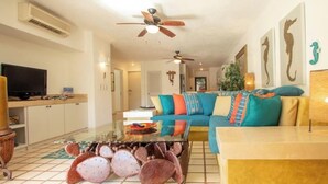 A living room with a sofa, coffee table, and a television. - Wrap-Around Patio & Pools · Terrasol Beach Resort (Cabo San Lucas)